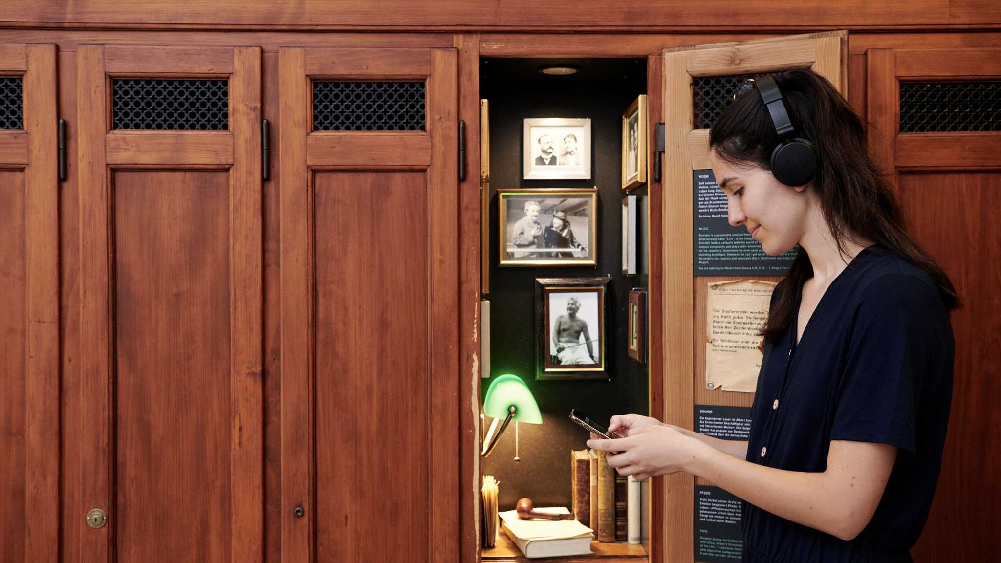 Eine Besucherin mit Handy und Kopfhörern vor dem Spind von Albert Einstein