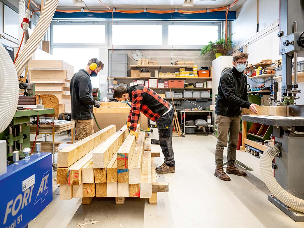 Drei junge Männer verarbeiten Holzbalken in einer Werkstatt