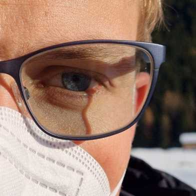 Nahaufnahme eines Gesichtes eines Mannes mit FFP2-Maske und Brille im Winter. Sein rechtes Brillenglas ist beschlagen. 