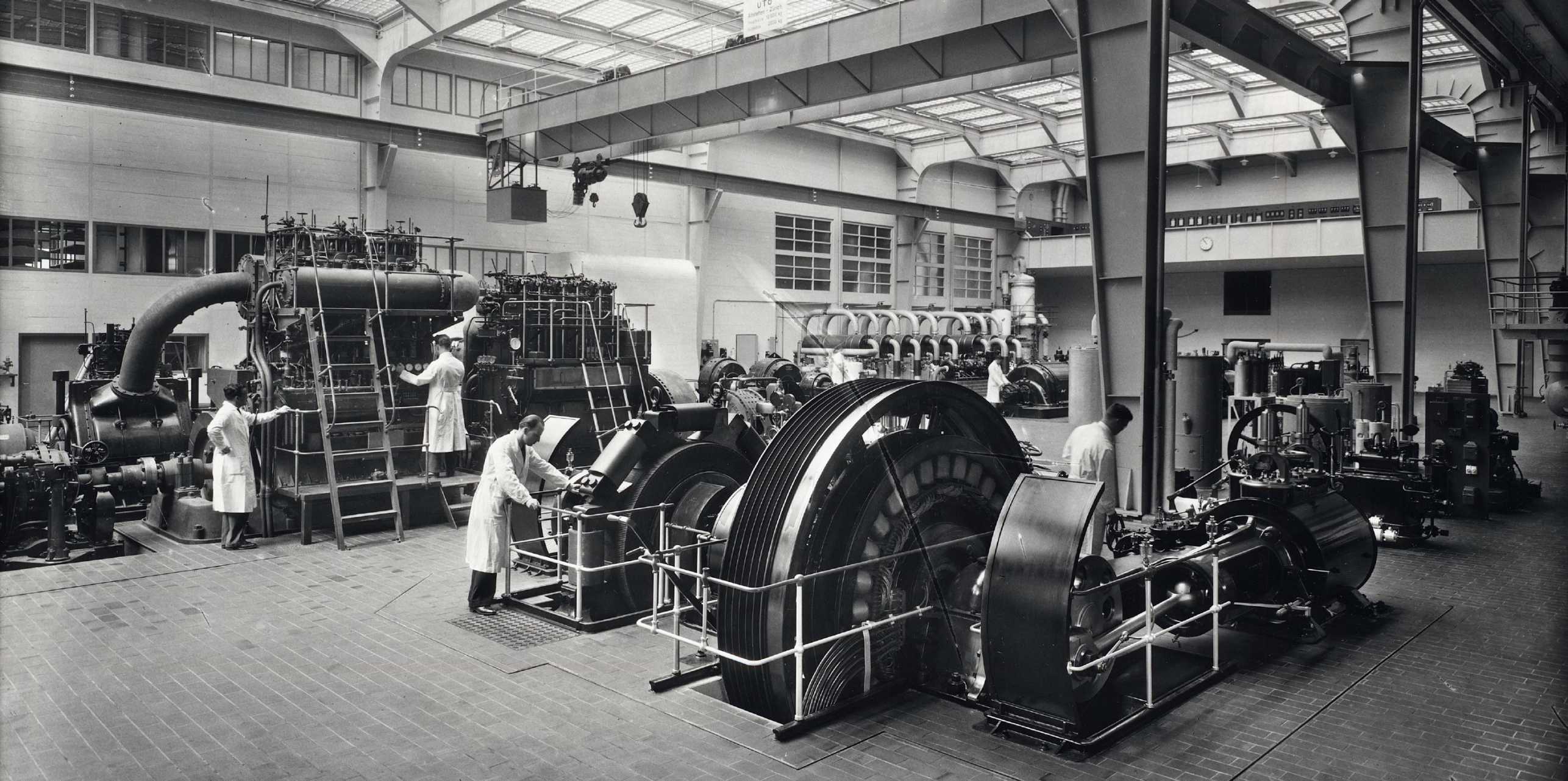 Altes schwarz weiss Bild einer Werkhalle, Personen beim Hantieren an den Maschinen.