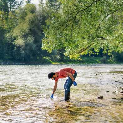 Mann steht im Fluss und entnimmt Wasserprobe