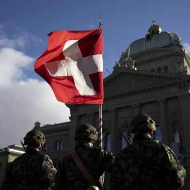 Drei Soldaten in Militärkleidung stehen vor dem Bundeshaus mit einer Fahne der Schweiz.