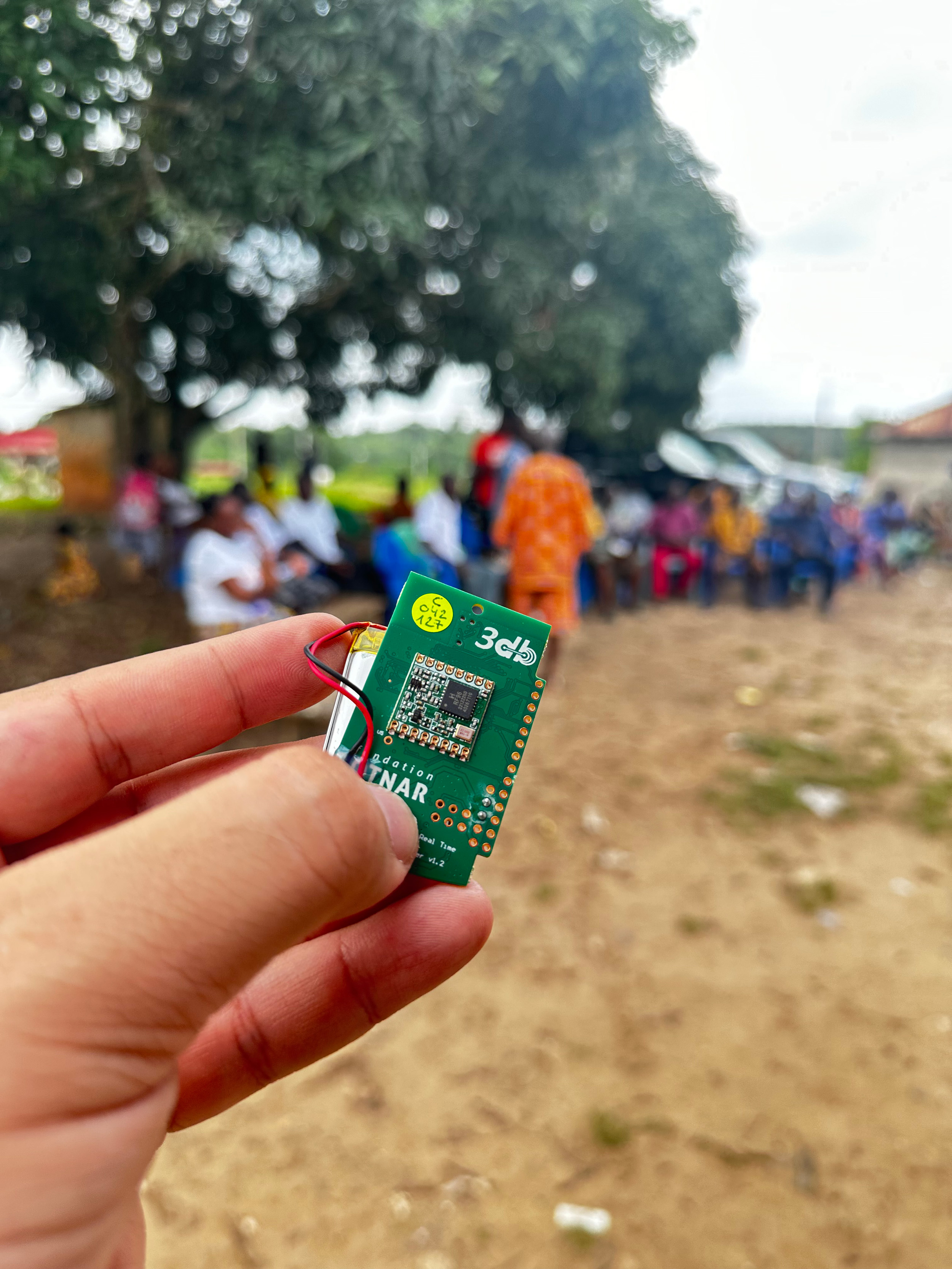 Vergr?sserte Ansicht: Hand welche den kleinen grünen Sensor hält, im Hintergrund ist ein afrikanisches Dorf erkennbar.