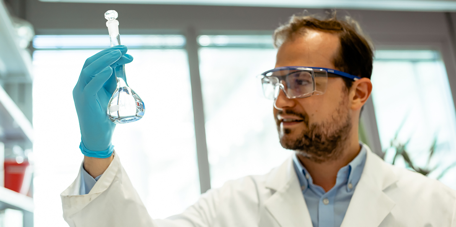 Dr. Maximilian Moser im Labor mit einer Flasche in der Hand