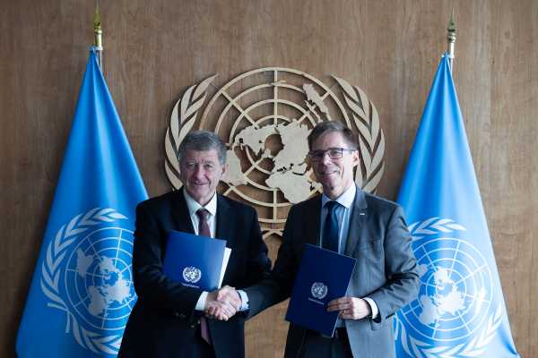 Guy Ryder, pictured left, and Jo?l Mesot shaking hands. They are each holding a blue folder, with the UN emblem in the background