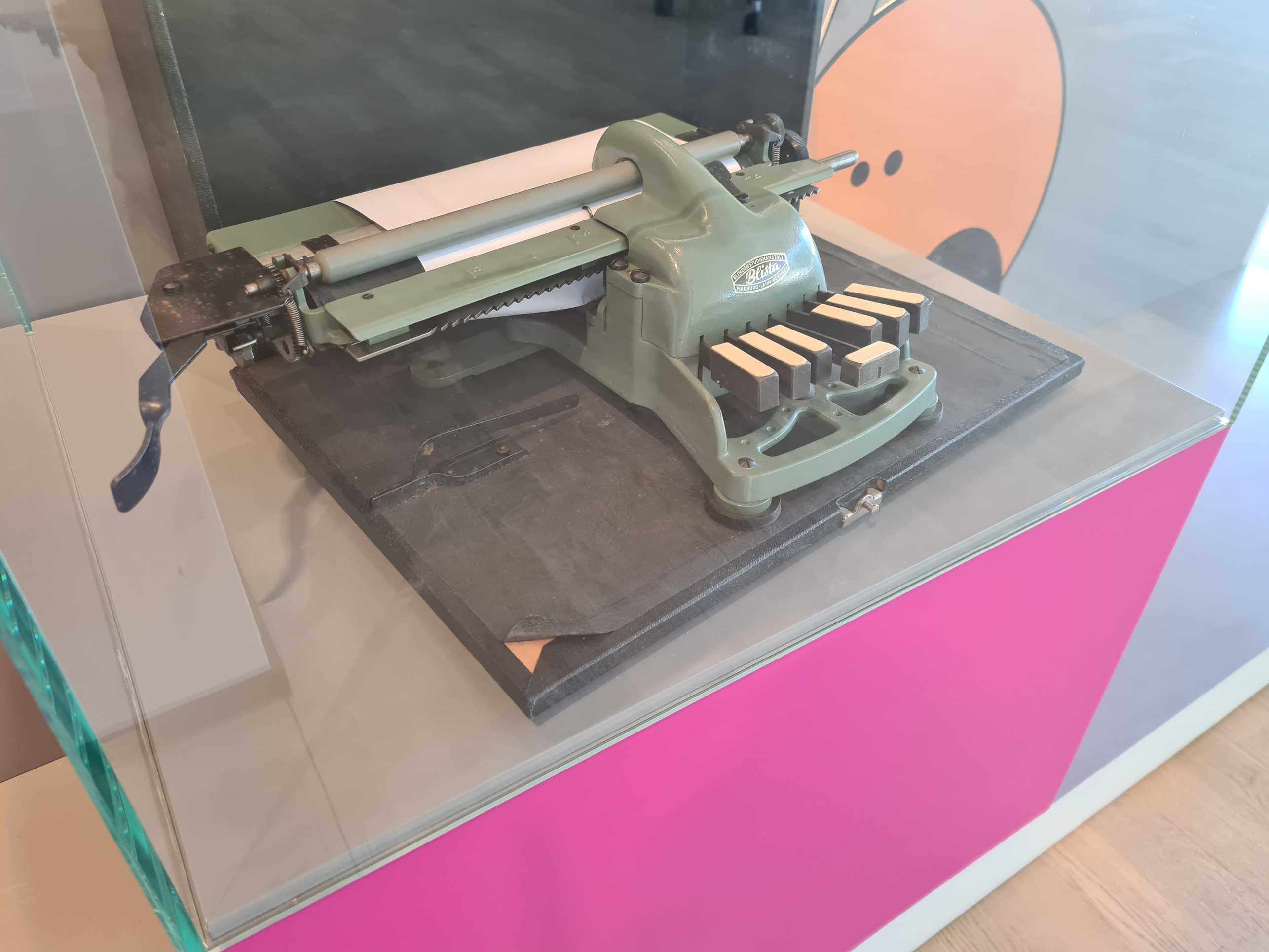 Eine alte Braille-Schreibmaschine steht hinter Glas.