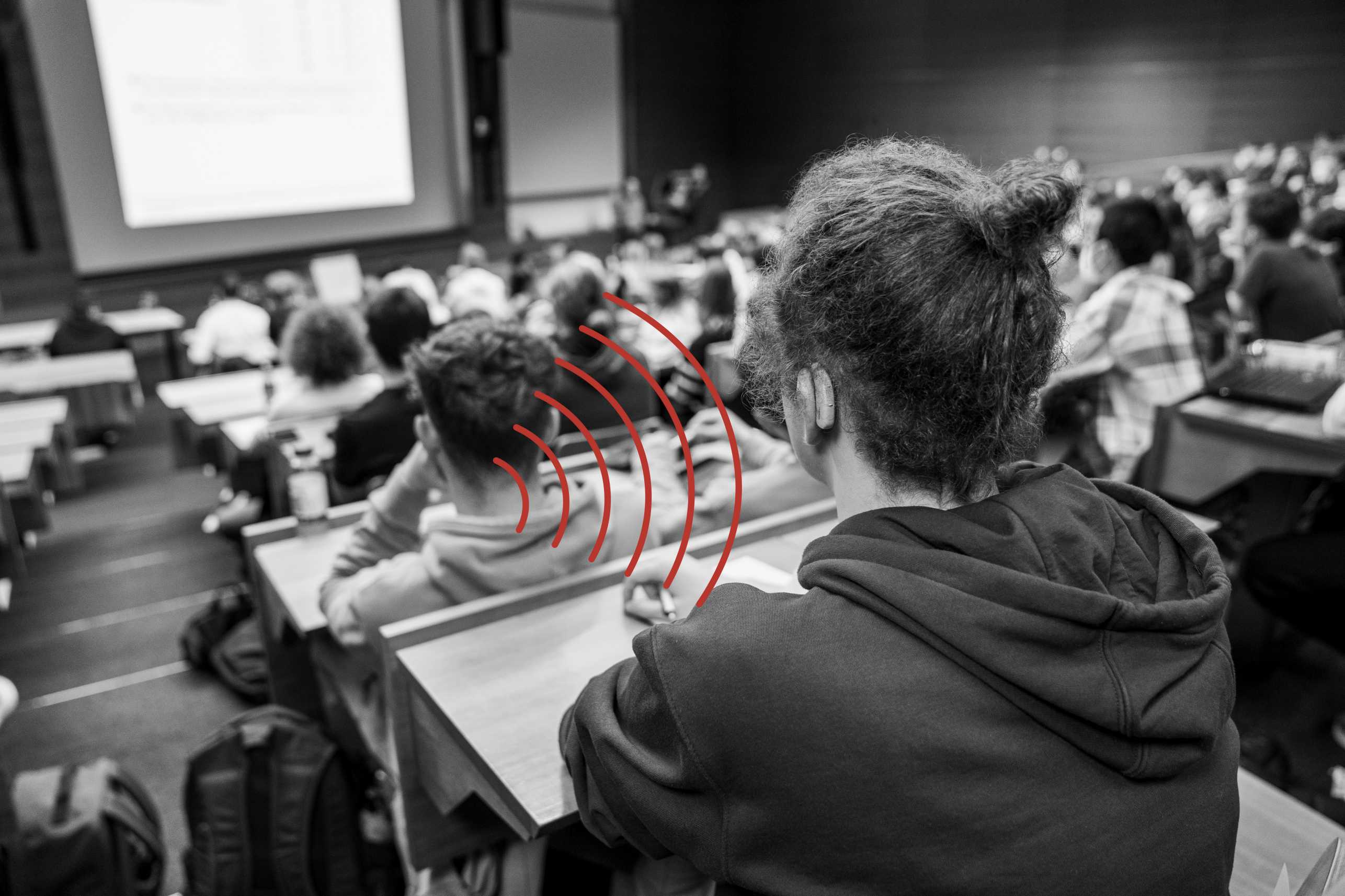 Vergr?sserte Ansicht: In einem Hörsaal voller Studierenden sitzt ein Student mit einem Hörgerät, welches die akustischen Signale über eine Induktionsschlaufe aufnimmt. 
