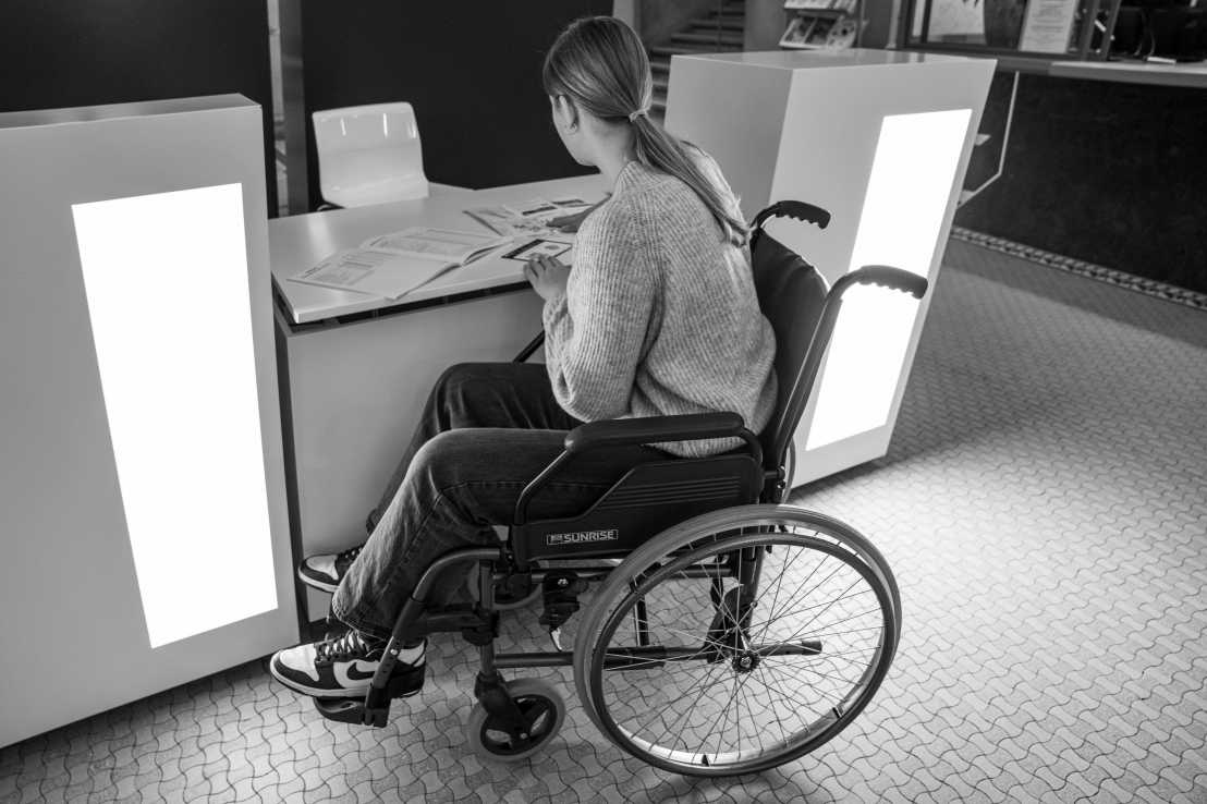 Eine Frau im Rollstuhl ist an einen barrierefreien Registrationsdesk gefahren. 