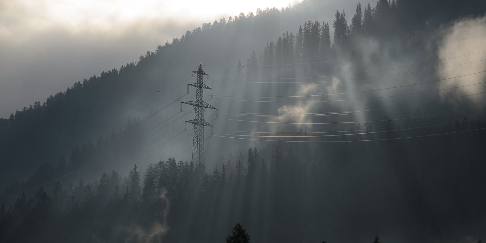 Stromnetz mit Strommast in den Schweizer Alpen, umgeben von Licht und Nebel