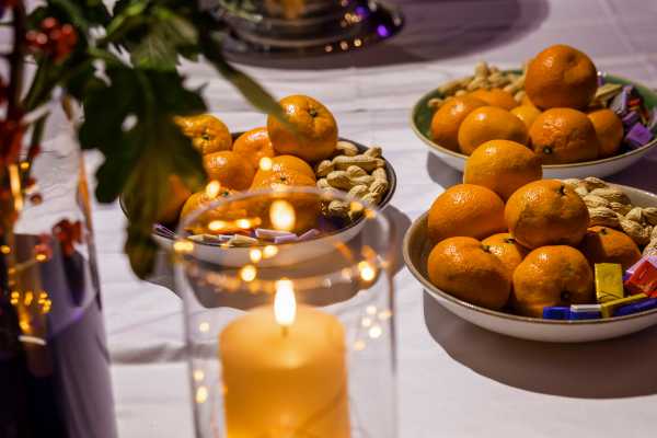 Tisch mit Teller voll Mandarinen und Nssen und stimmungsvollen Kerzen.
