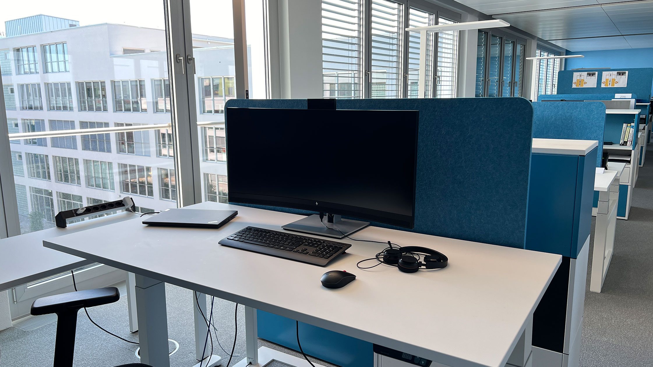 IT-Ausstattung eines künftigen Desk-Sharing-Arbeitsplatzes: Curved-Docking-Monitor mit Webcam, Notebook, Tastatur, Maus sowie Headset.